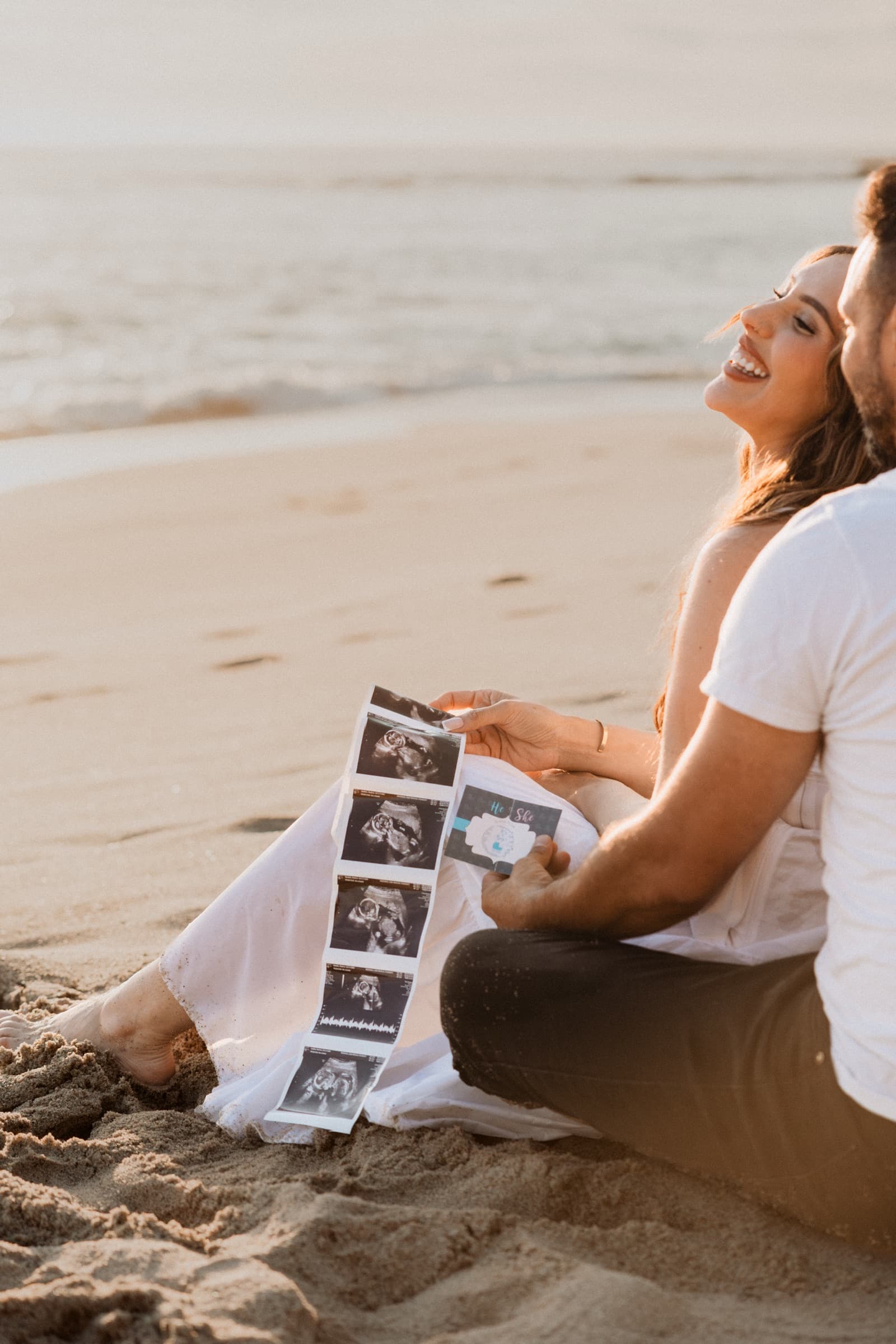 Couple laughing with their sonogram on the sand