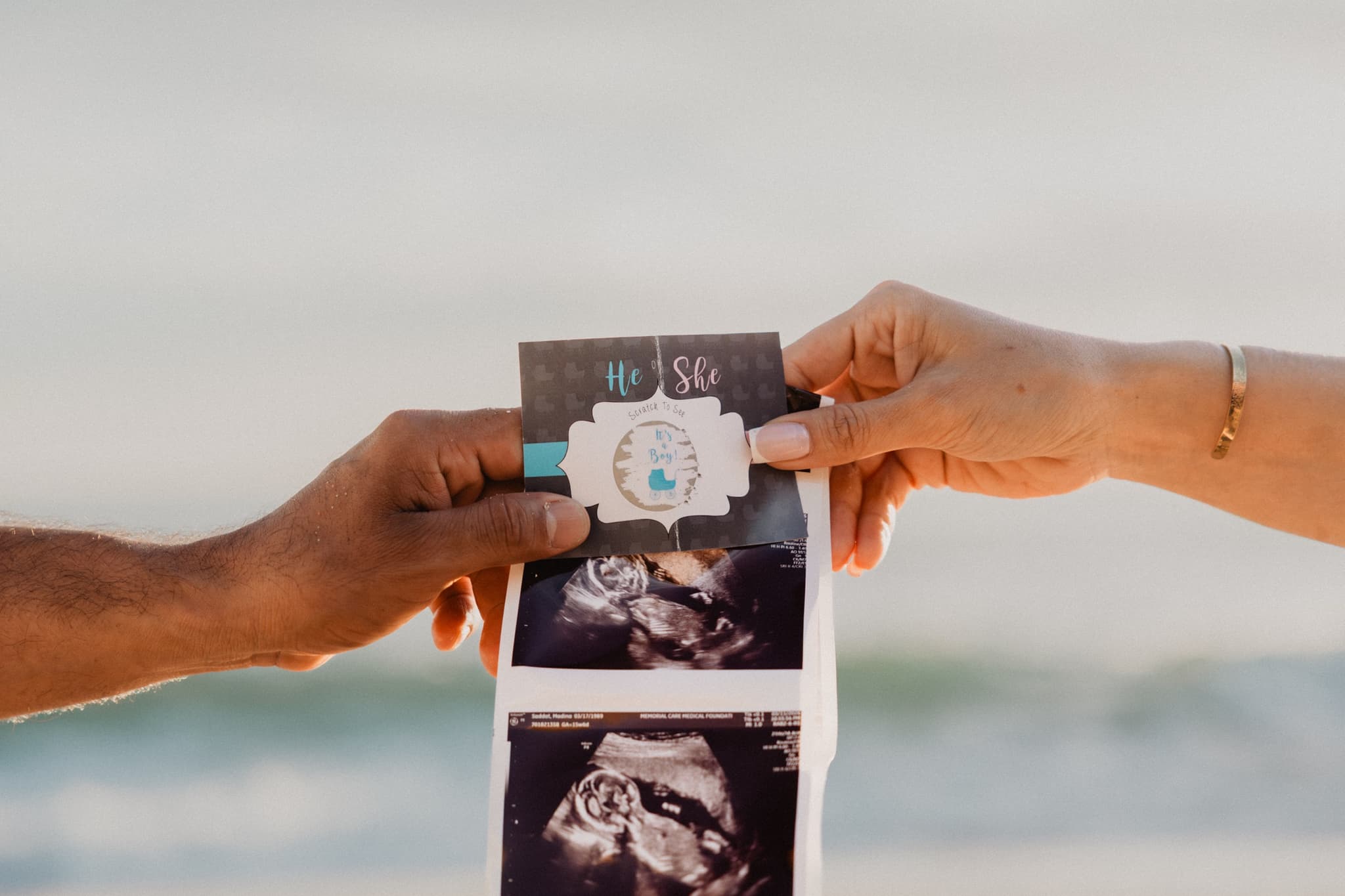 Hands holding the sonogram against the ocean