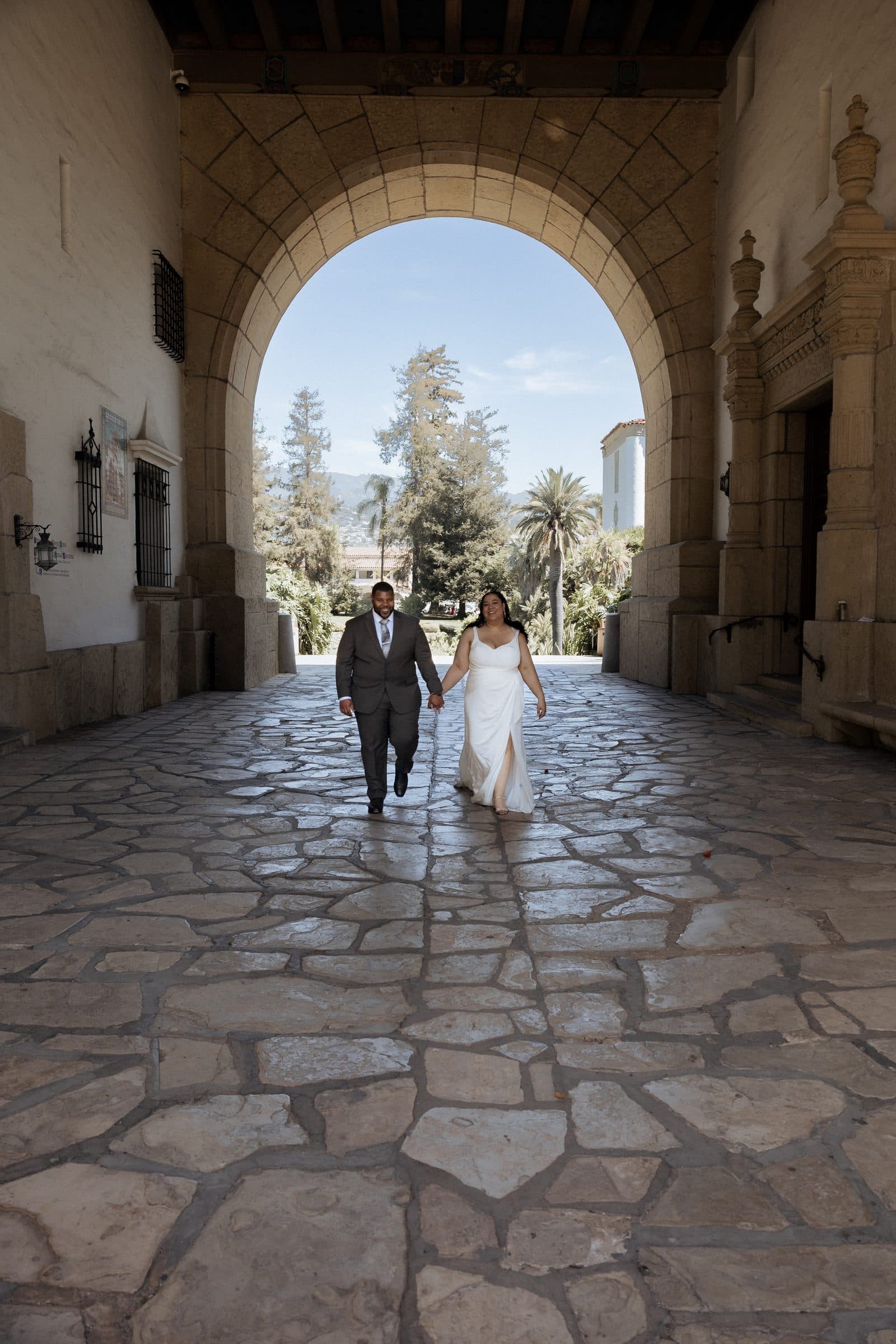 Couple walking through the stone arch corridor of the Santa Barbara County Courthouse