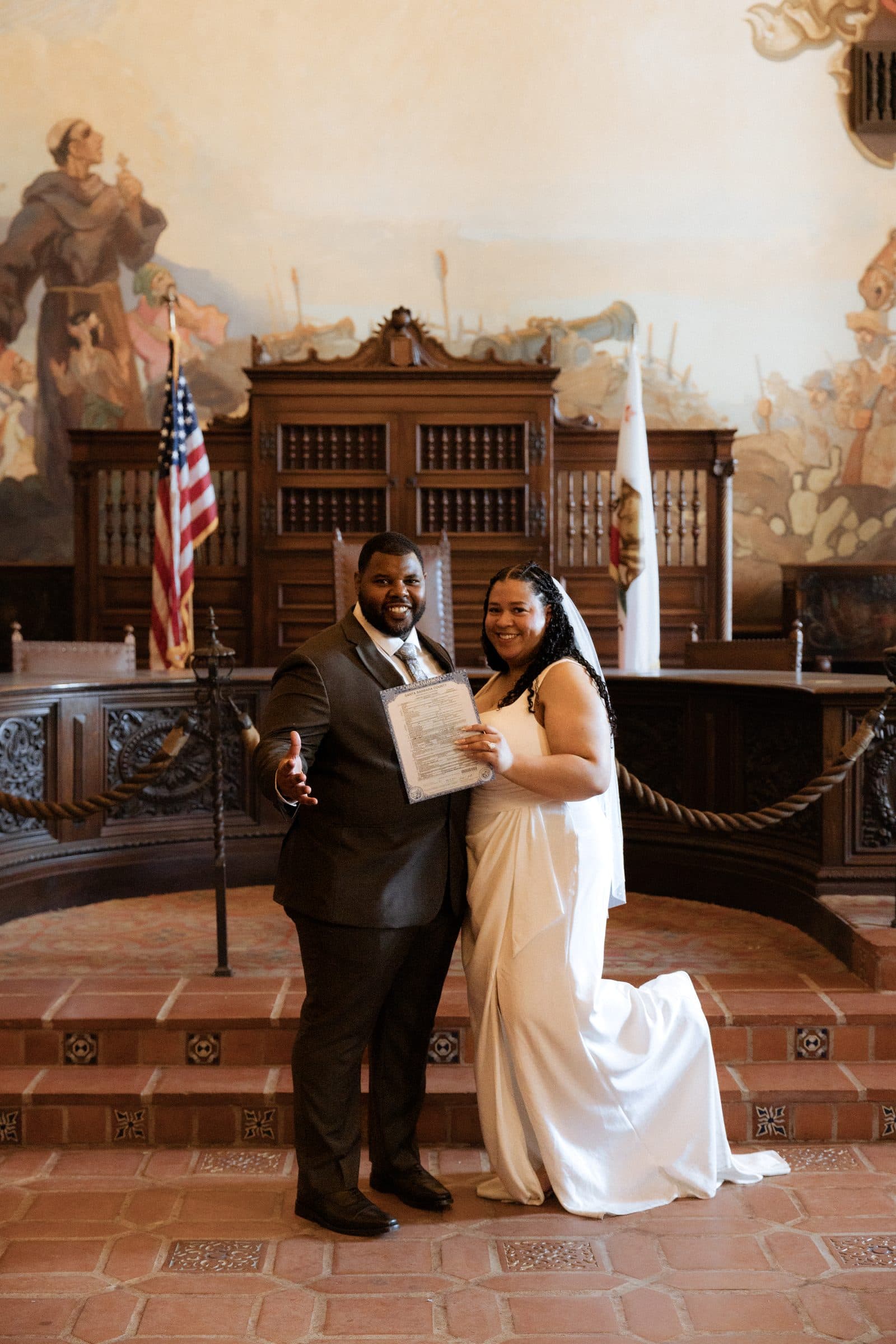 Couple holding their marriage license in the Mural Room of the Santa Barbara County Courthouse