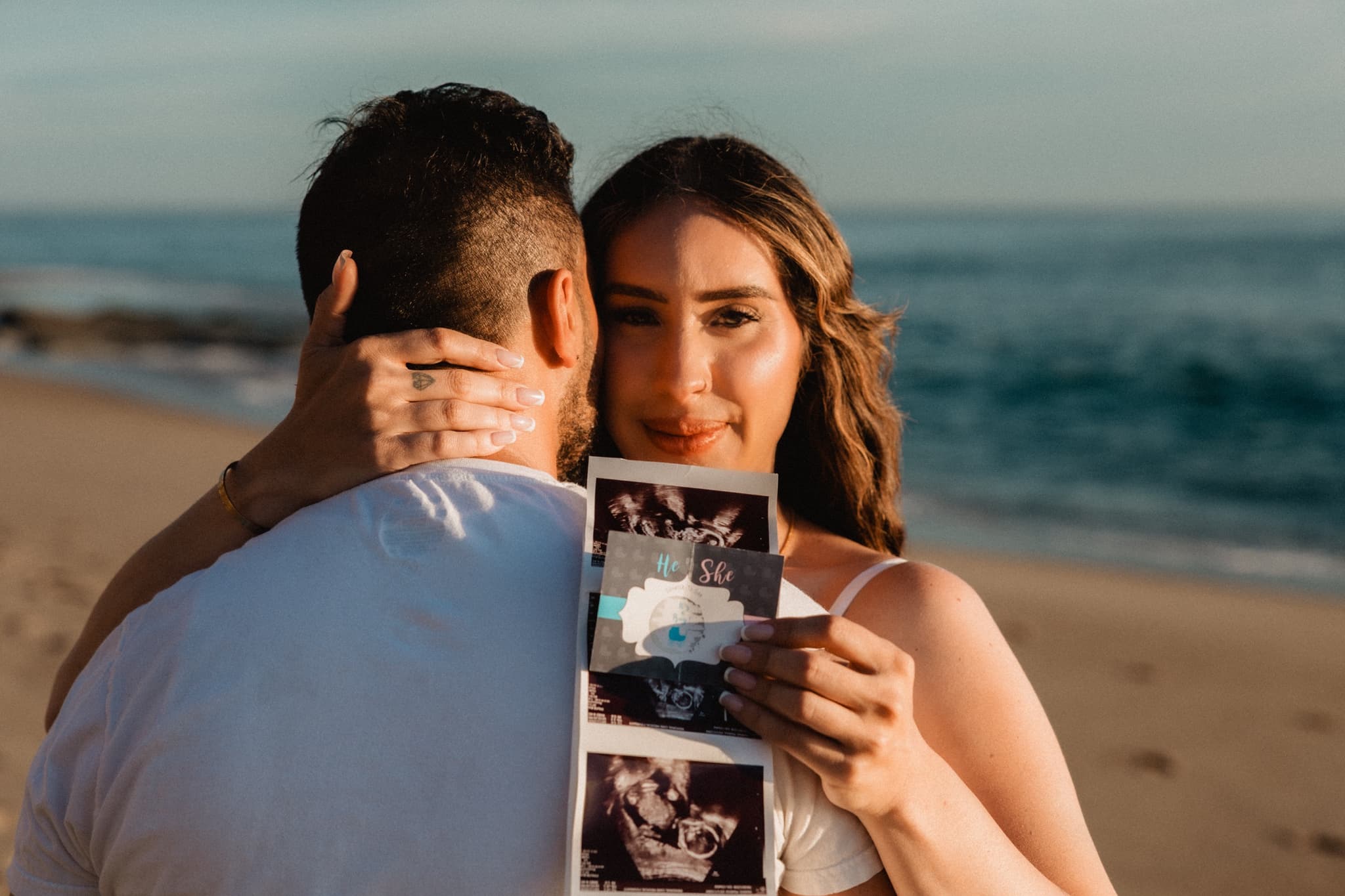 Couple holding their sonogram at the beach — Southern California gender reveal session