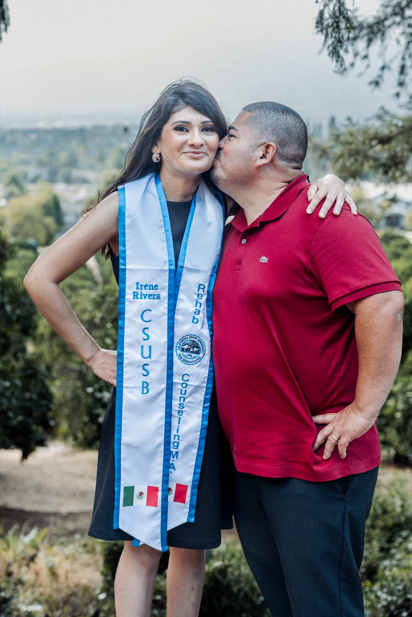 A father kissing his daughter on the cheek, her CSUSB graduation stole around her shoulders
