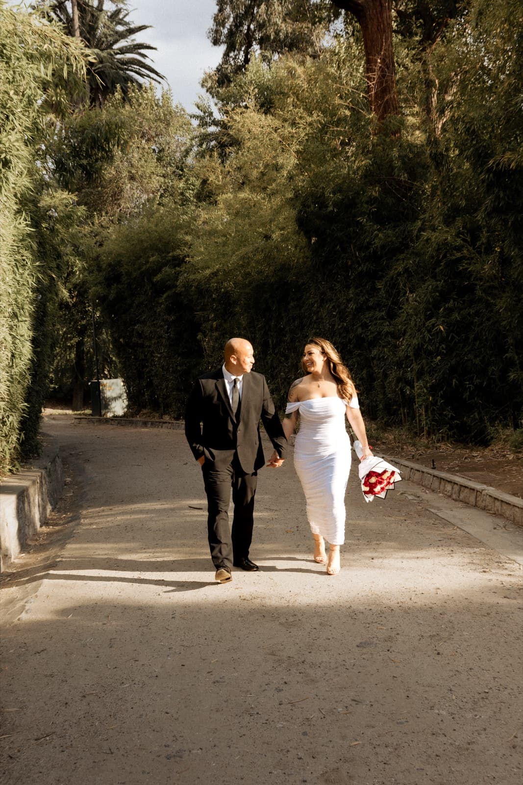 Groom leading his bride down a tree-lined path after their courthouse wedding