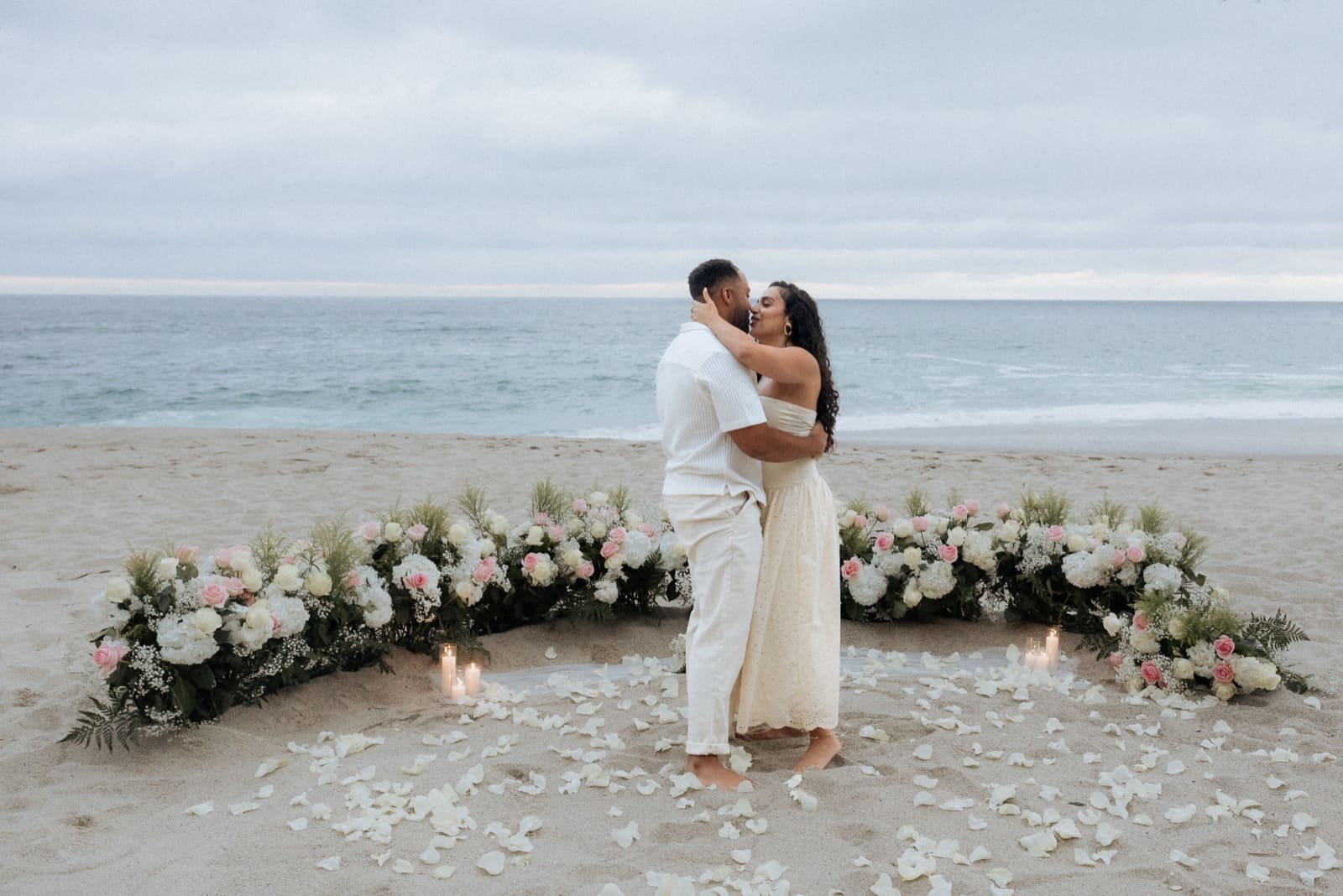 Couple under a floral arch on the beach at golden hour