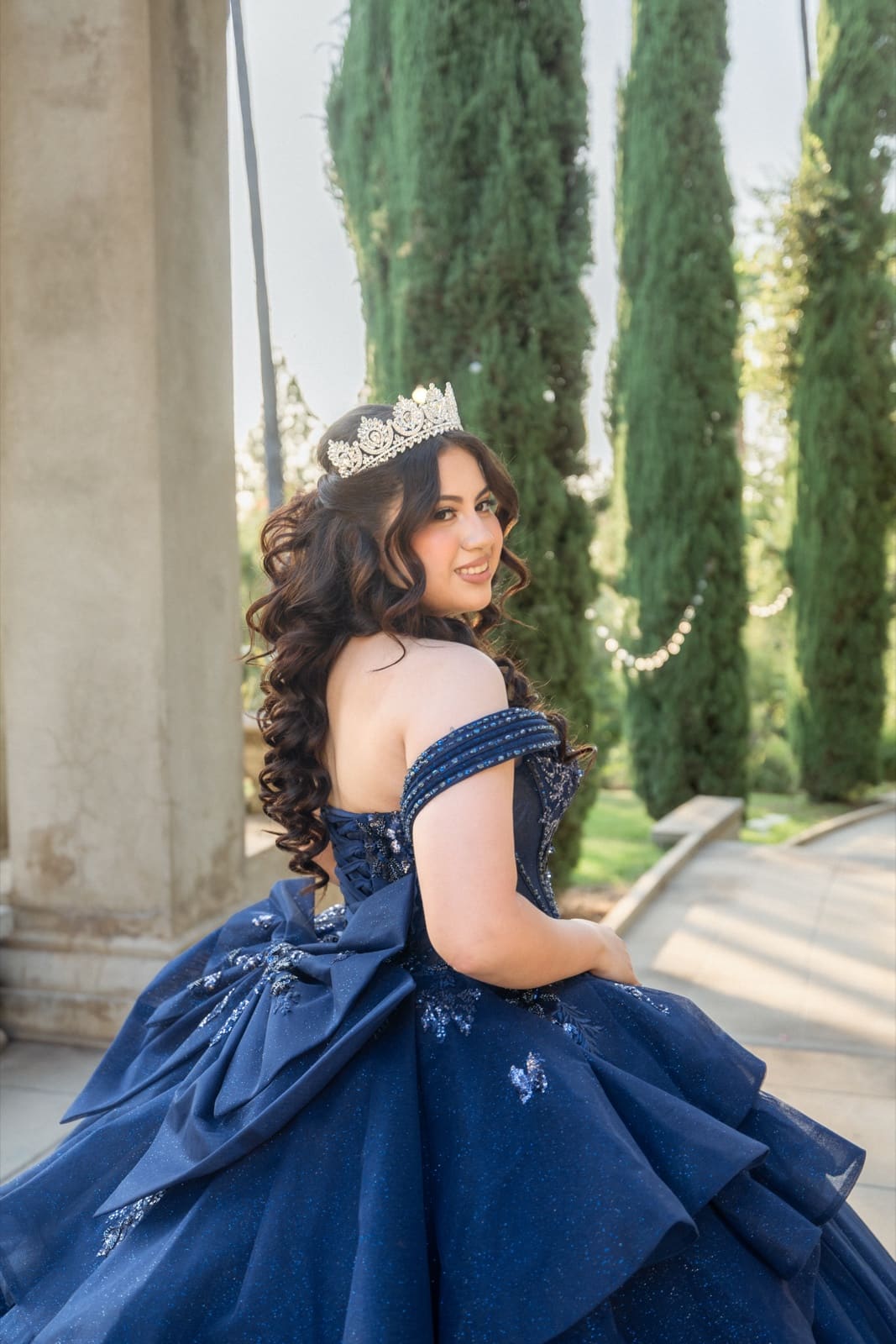 Quinceañera portrait — crown and curls, seated under a pergola