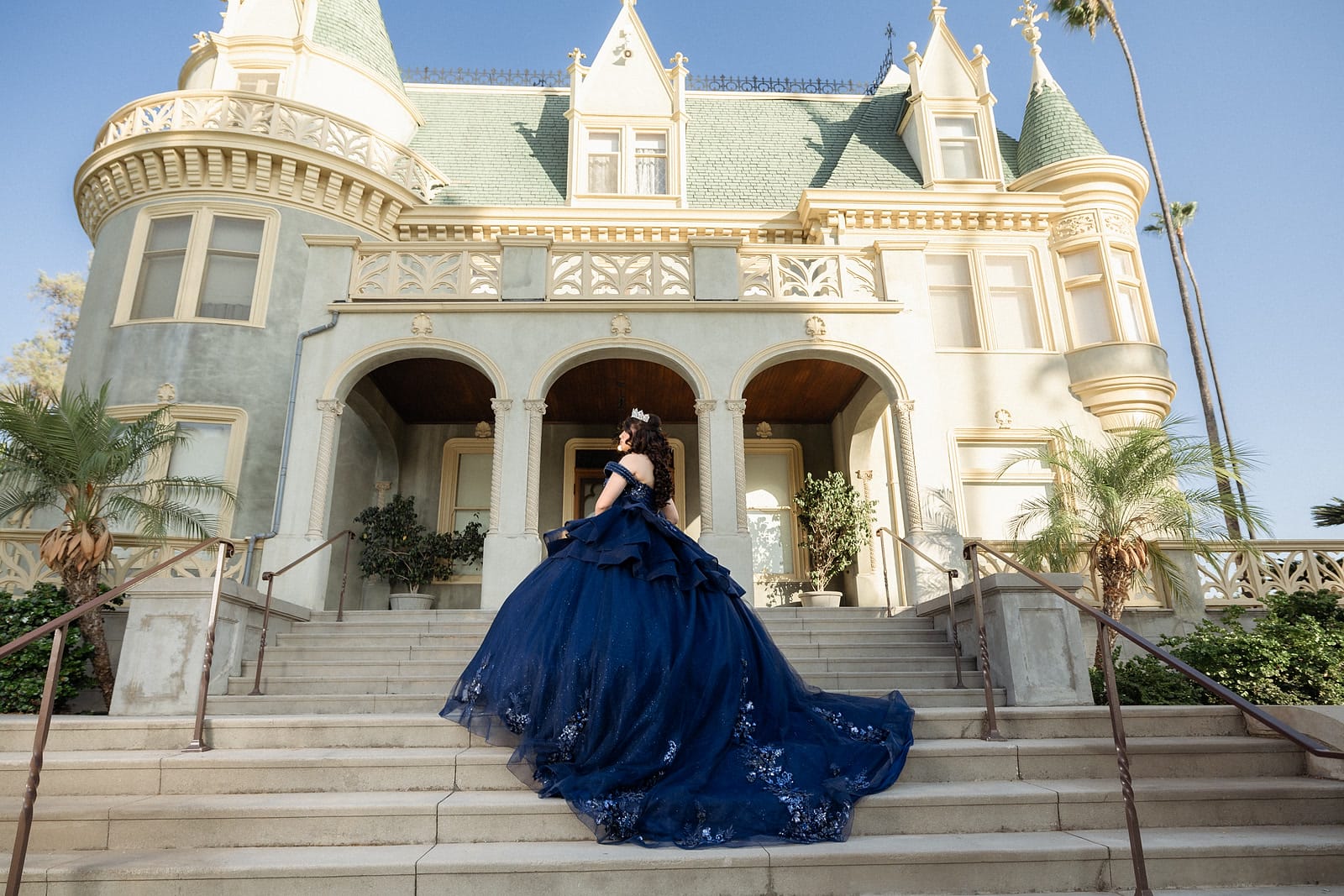 Quinceañera in a navy ball gown on the steps of Kimberly Crest House, Redlands